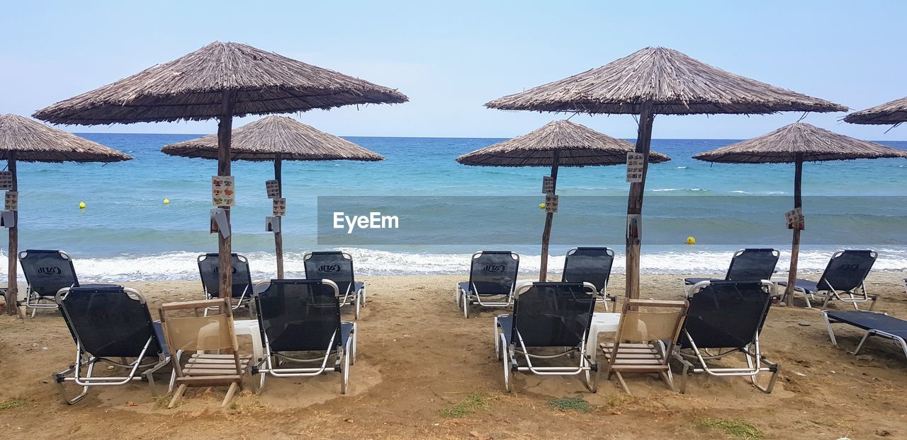 Deck chairs on beach against sky