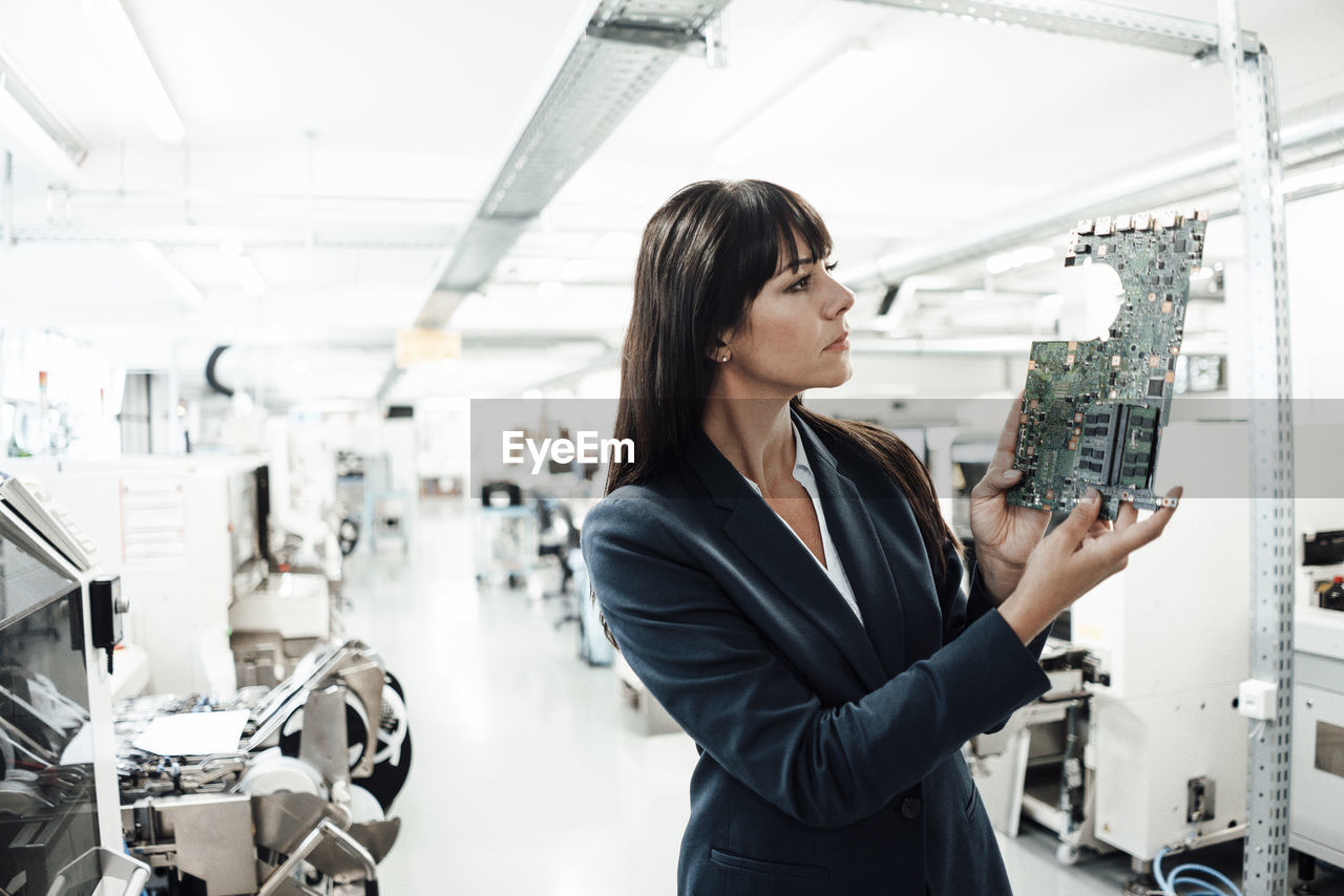 Businesswoman investigating while looking at circuit board in industry