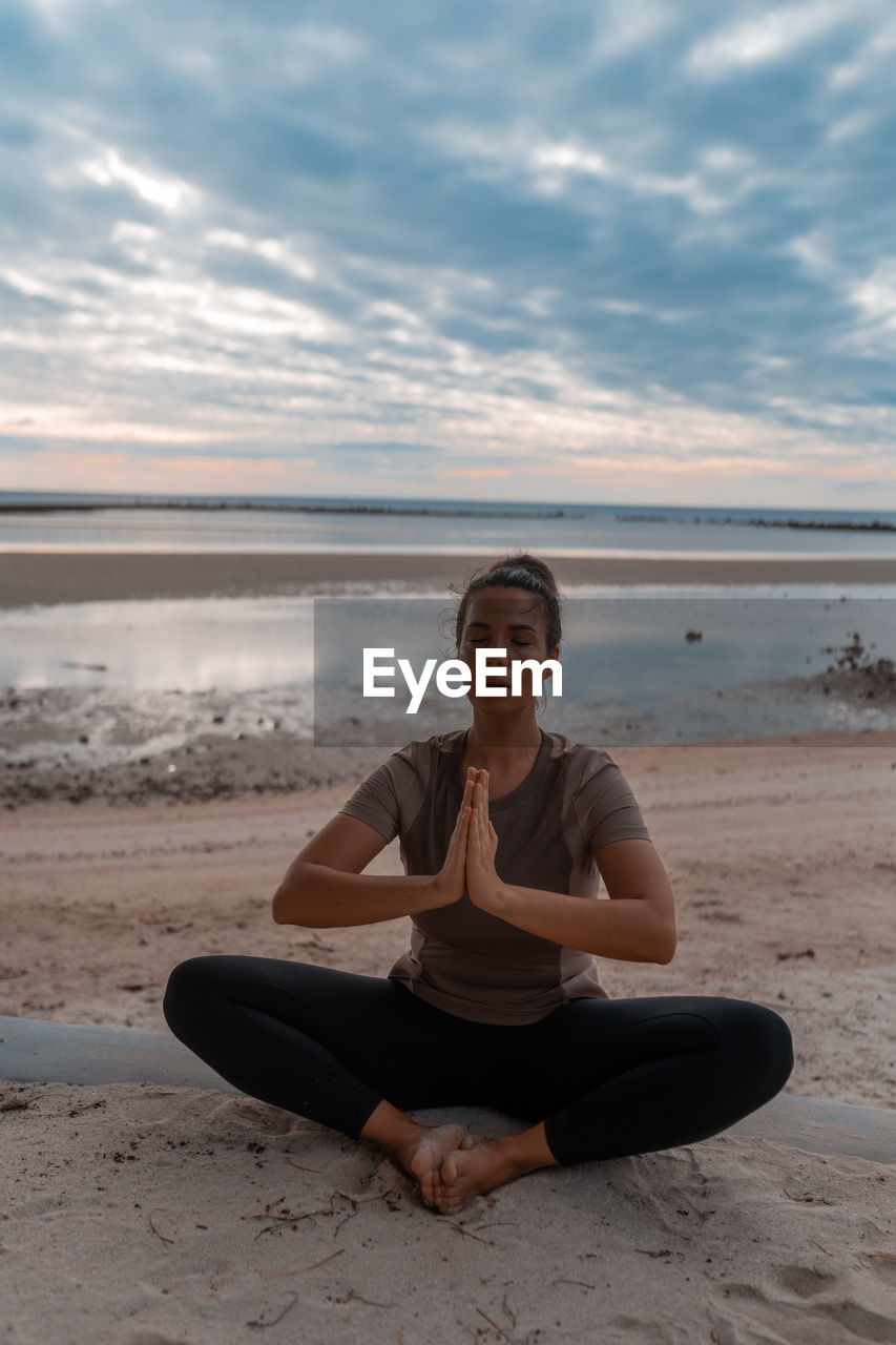 Portrait of young woman sitting at beach against sky