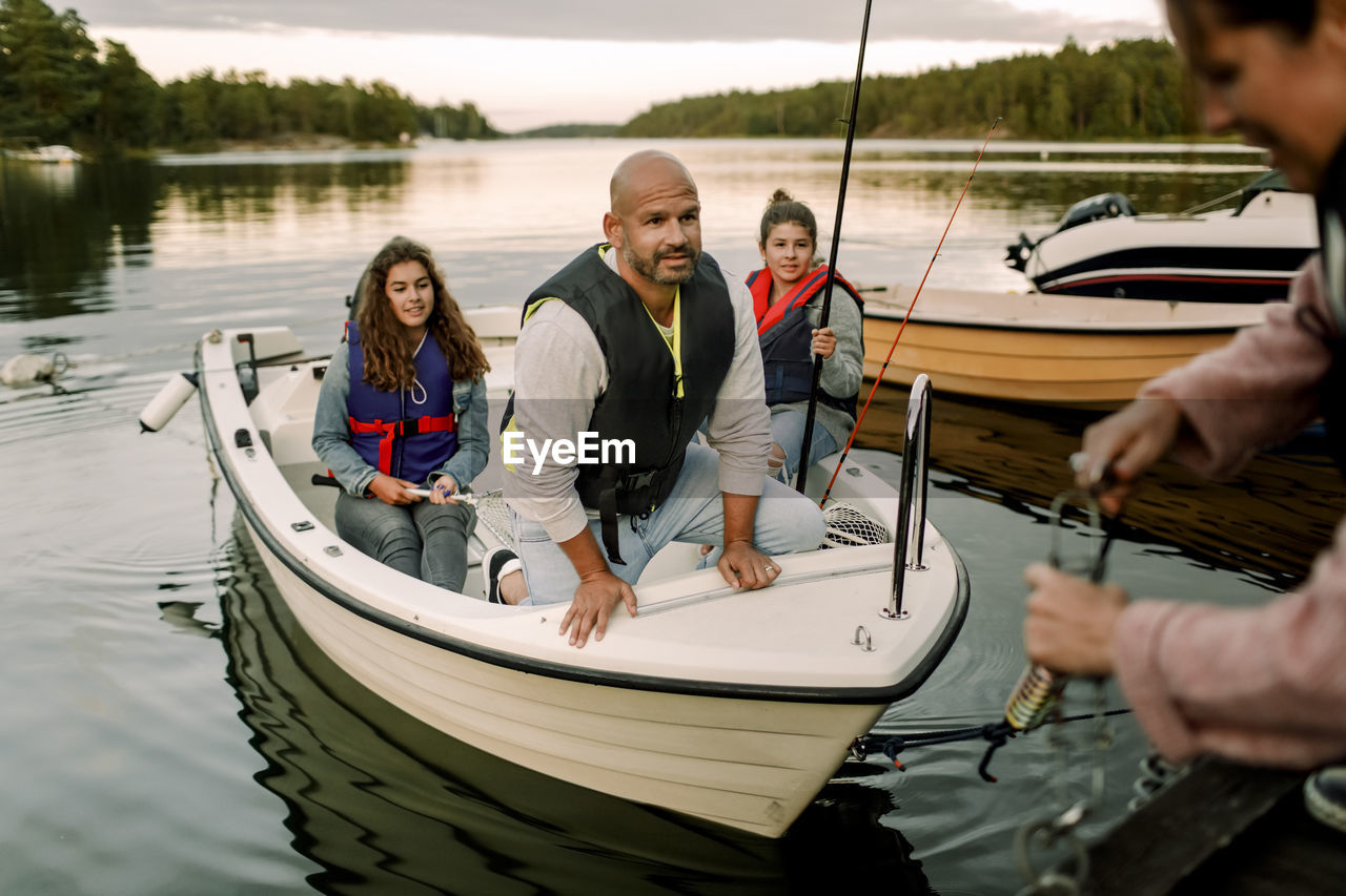 Family looking at woman anchoring boat near pier during sunset