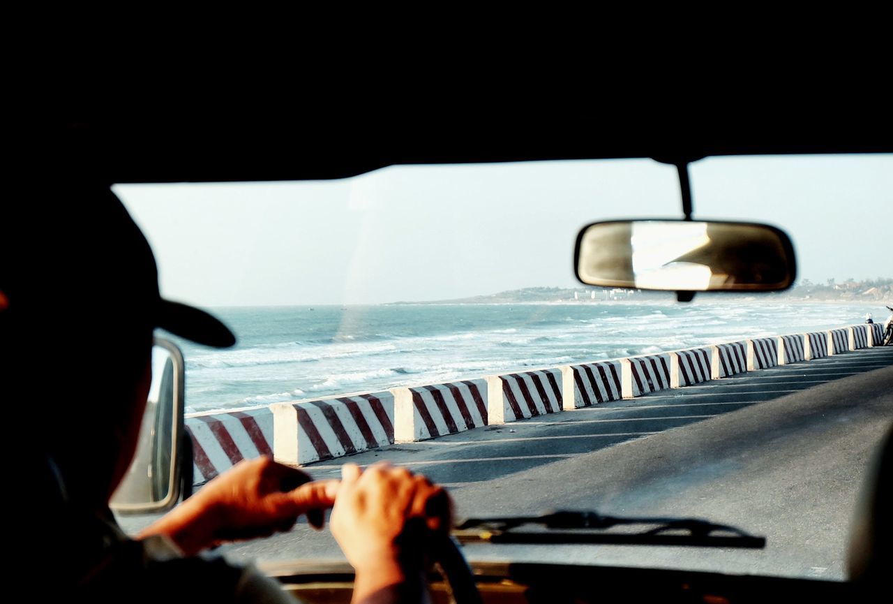 Close-up of man driving car on road against sea