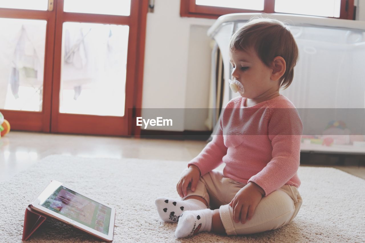 Cute girl looking at digital tablet on rug at home