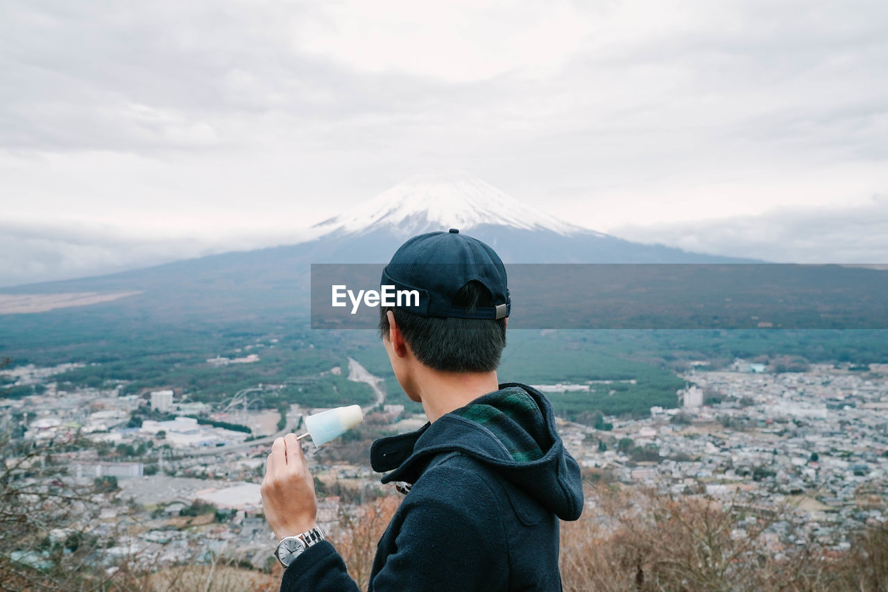 Side view of man wearing cap eating ice cream against mountain and sky