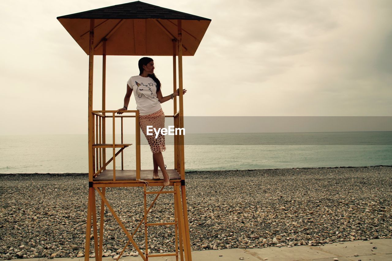 Full length of young woman standing in lifeguard hut at beach