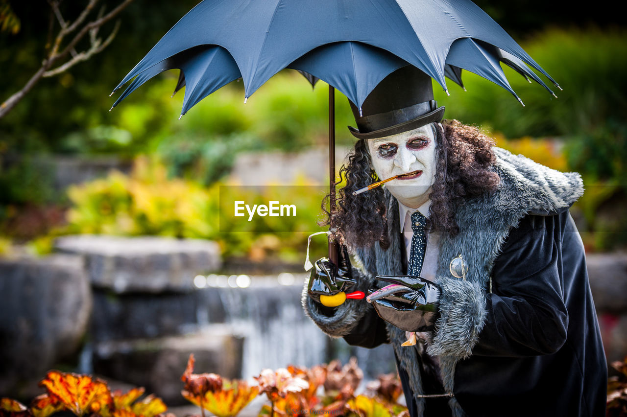 Portrait of man in costume smoking cigarette while holding umbrella