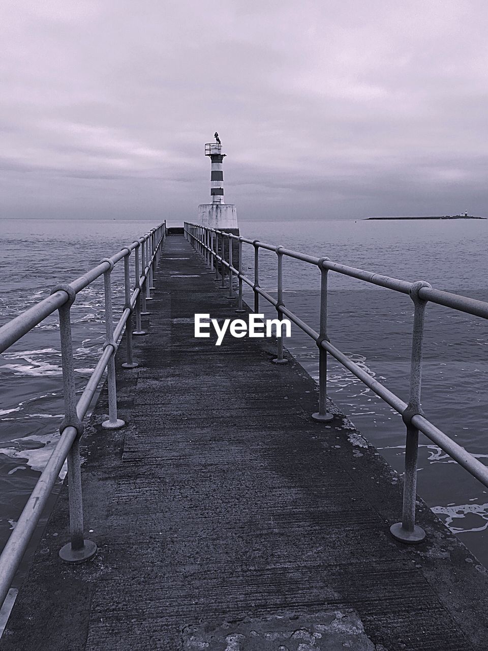 PIER LEADING TOWARDS LIGHTHOUSE AT SEA AGAINST SKY