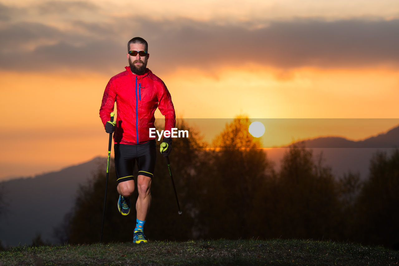 FULL LENGTH PORTRAIT OF MAN STANDING AGAINST SKY DURING SUNSET