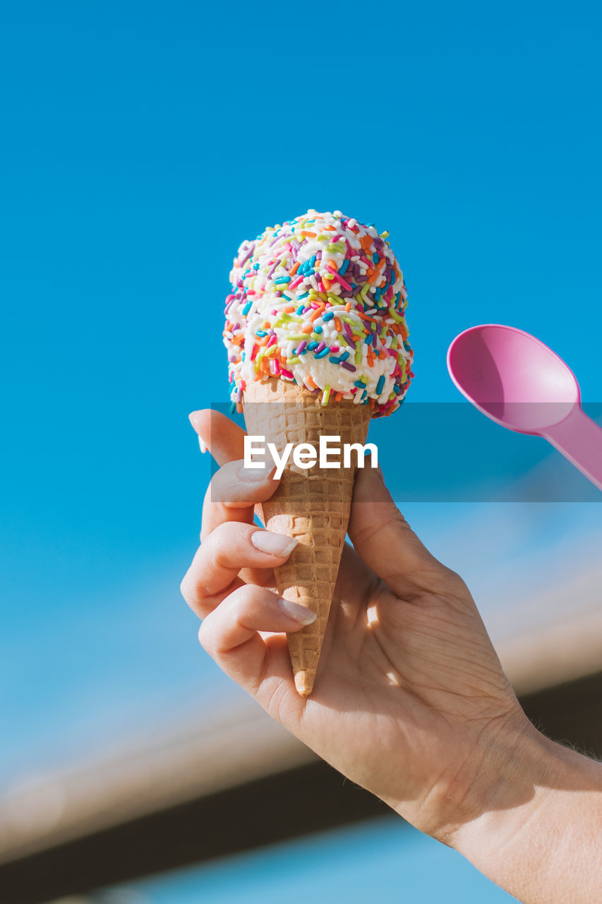 Cropped hand of woman holding ice cream against sky