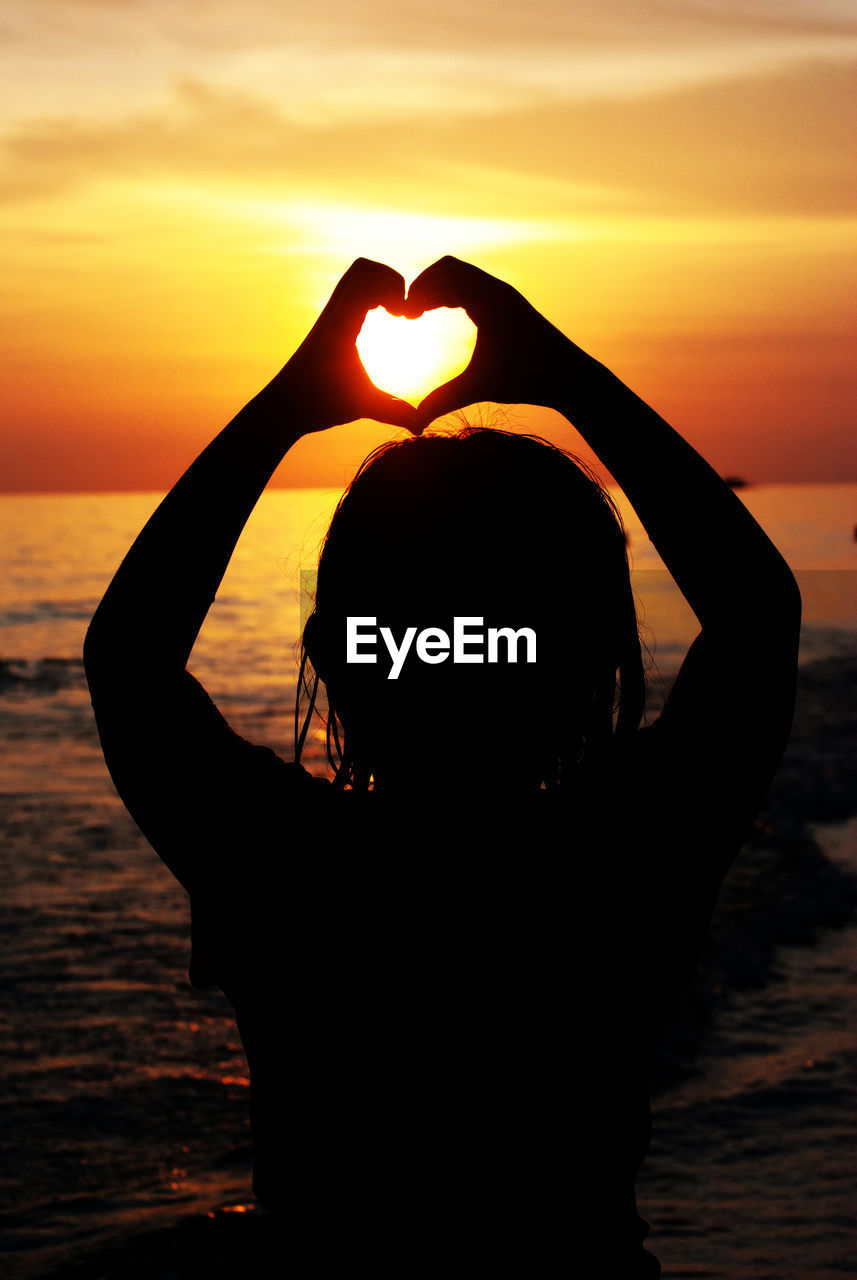 Silhouette woman making heart shape at beach against sky