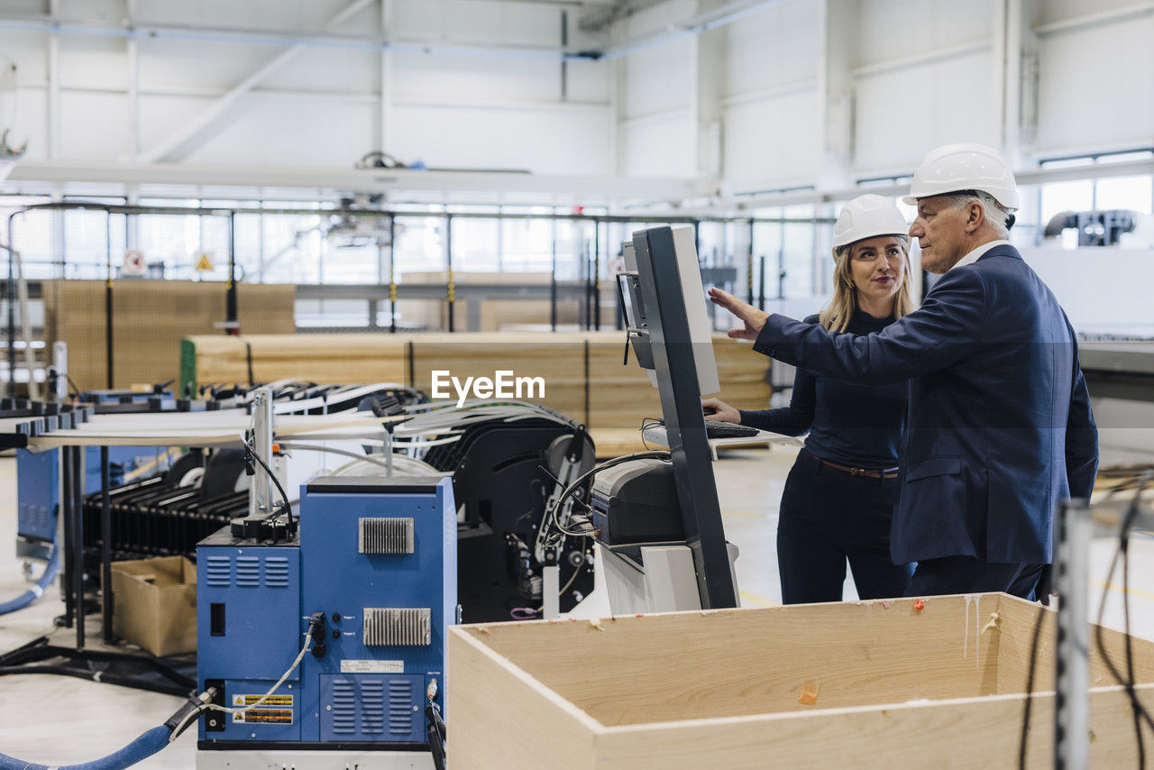 Manager explaining machine to colleague standing in factory