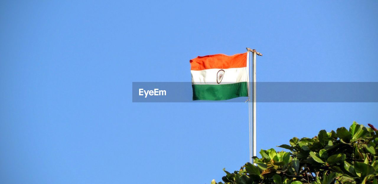 Low angle view of indian flag by tree against clear blue sky
