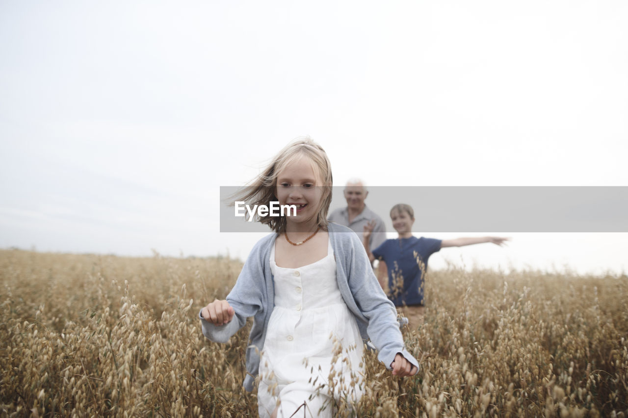 Portrait of happy girl running in an oat field while brother and grandfather following her