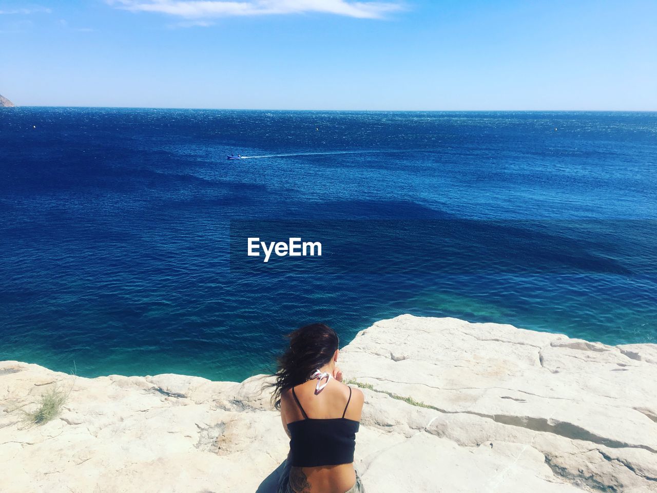 Rear view of woman sitting on rock against sea