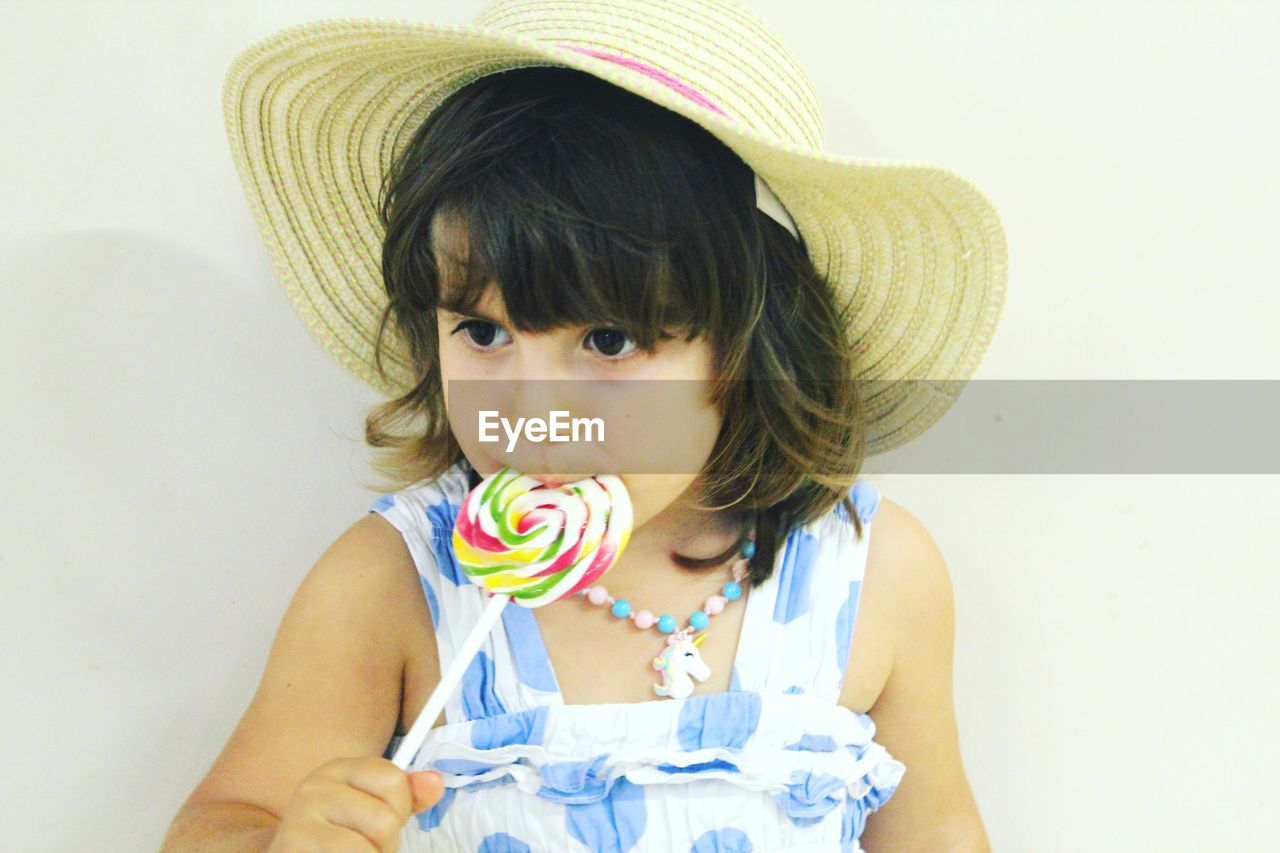 Close-up of cute girl eating lollipop against wall