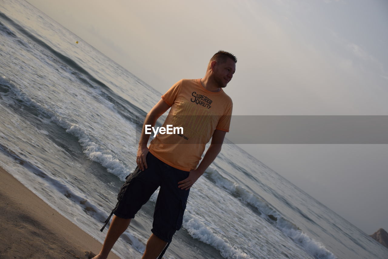 YOUNG MAN STANDING ON BEACH