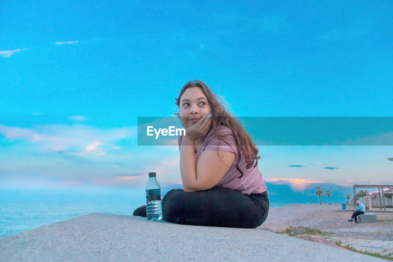 Portrait of young woman looking at sea against blue sky