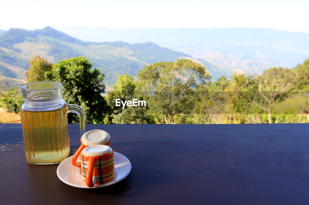 CLOSE-UP OF COFFEE CUP ON TABLE BY MOUNTAINS