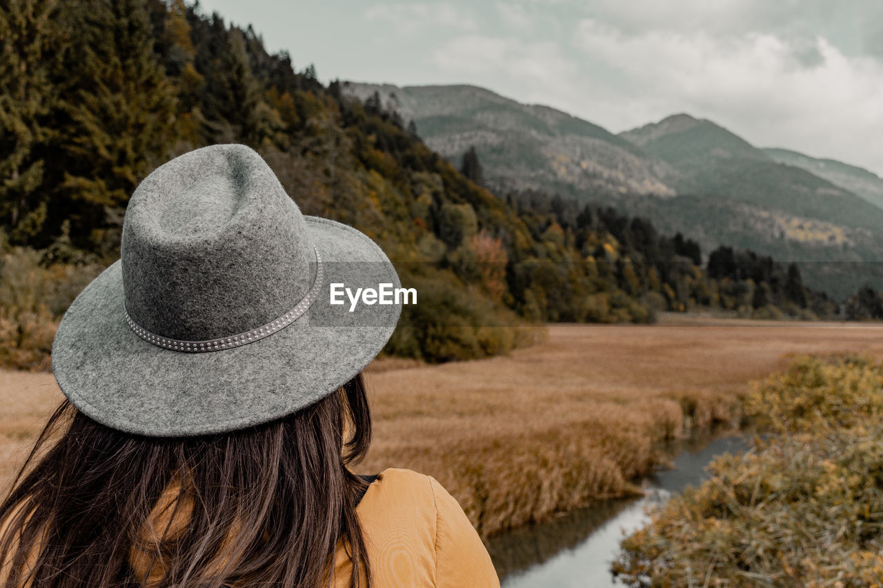 hat, landscape, mountain, one person, adult, nature, environment, rear view, clothing, land, scenics - nature, sky, women, plant, mountain range, leisure activity, beauty in nature, sun hat, cloud, rural scene, fashion accessory, wilderness, travel, tree, vacation, tranquility, travel destinations, long hair, holiday, water, tranquil scene, trip, outdoors, day, lifestyles, headshot, tourism, relaxation, portrait, hairstyle, remote, non-urban scene, forest
