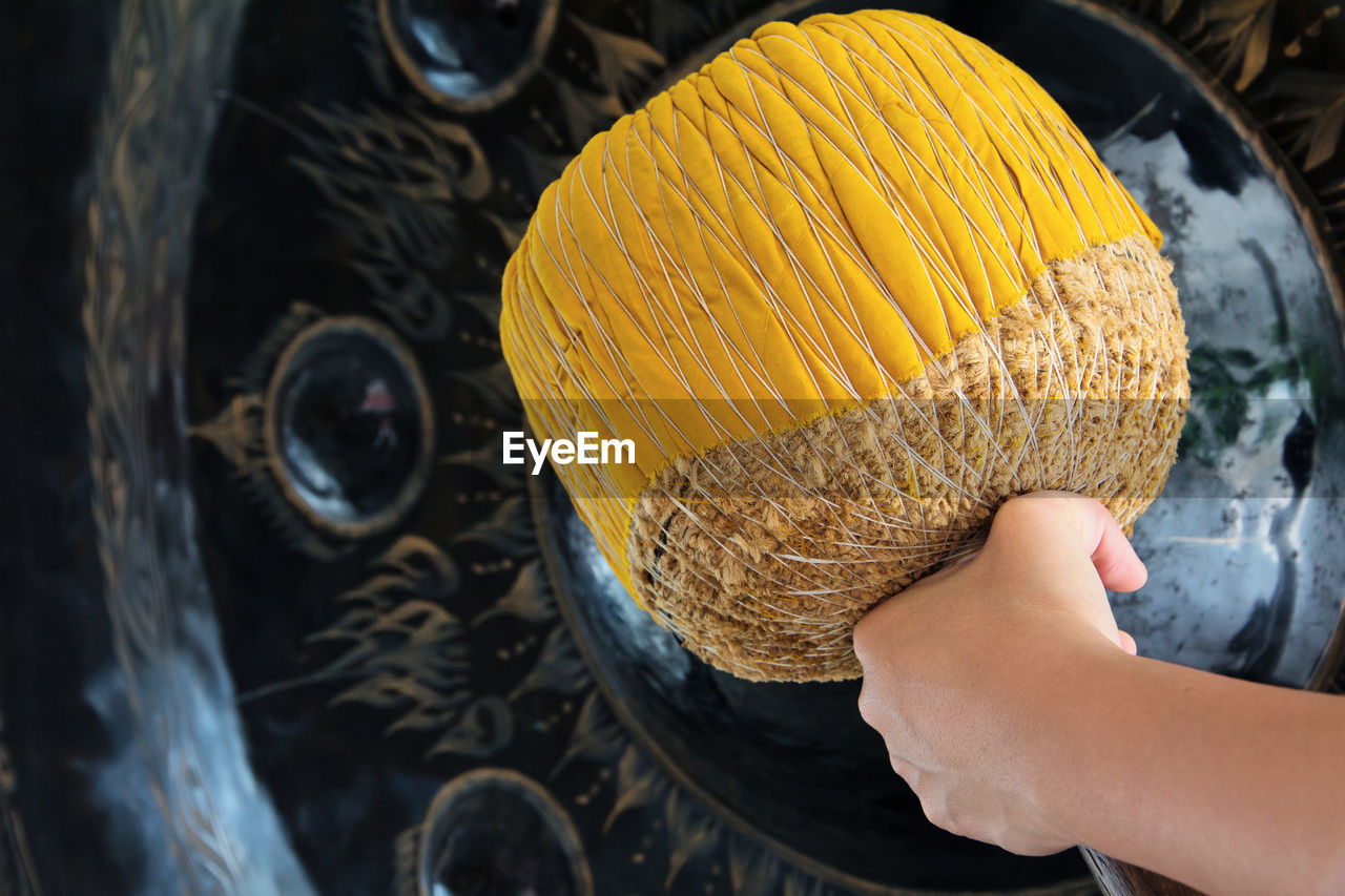 Midsection of woman banging gong with yellow mallet