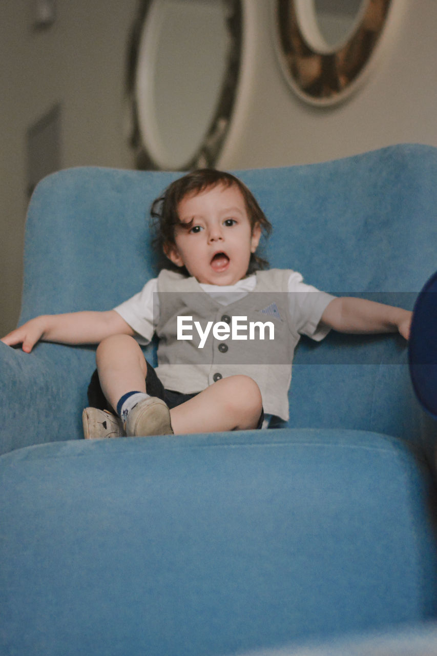 2 years toddler sitting on the chair with an open mouth at home 