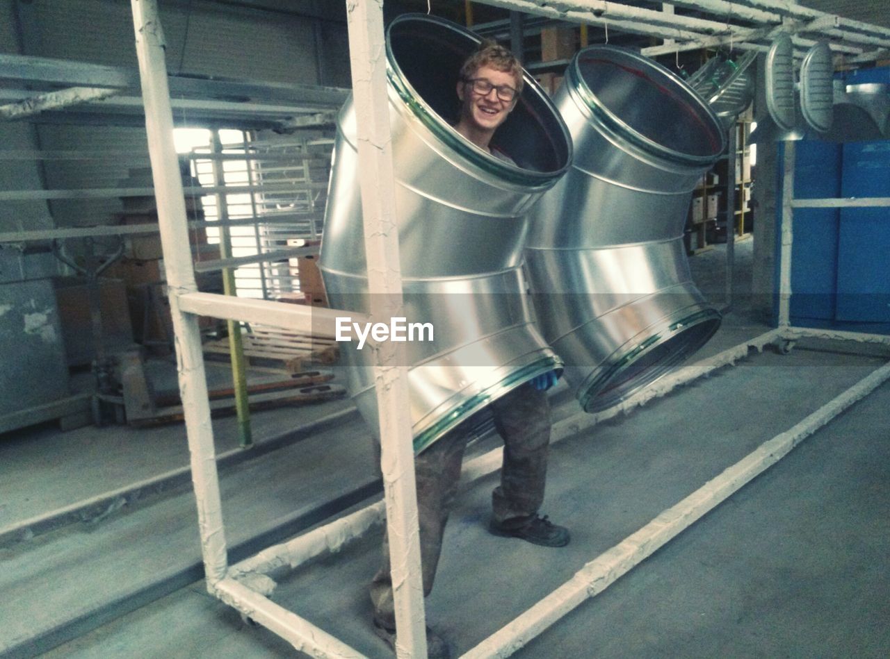 Happy young man standing in pipe at factory