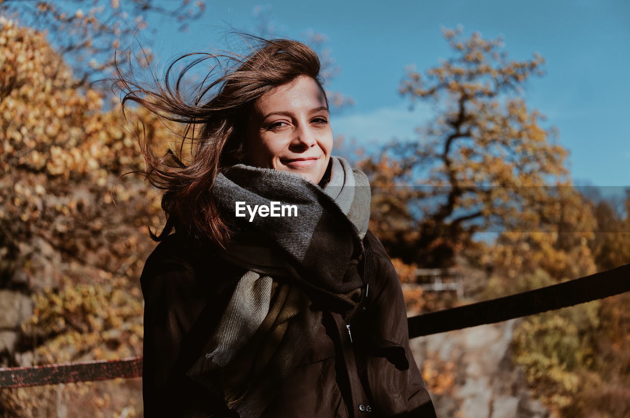 Portrait of smiling young woman wearing warm clothing while standing in forest during autumn