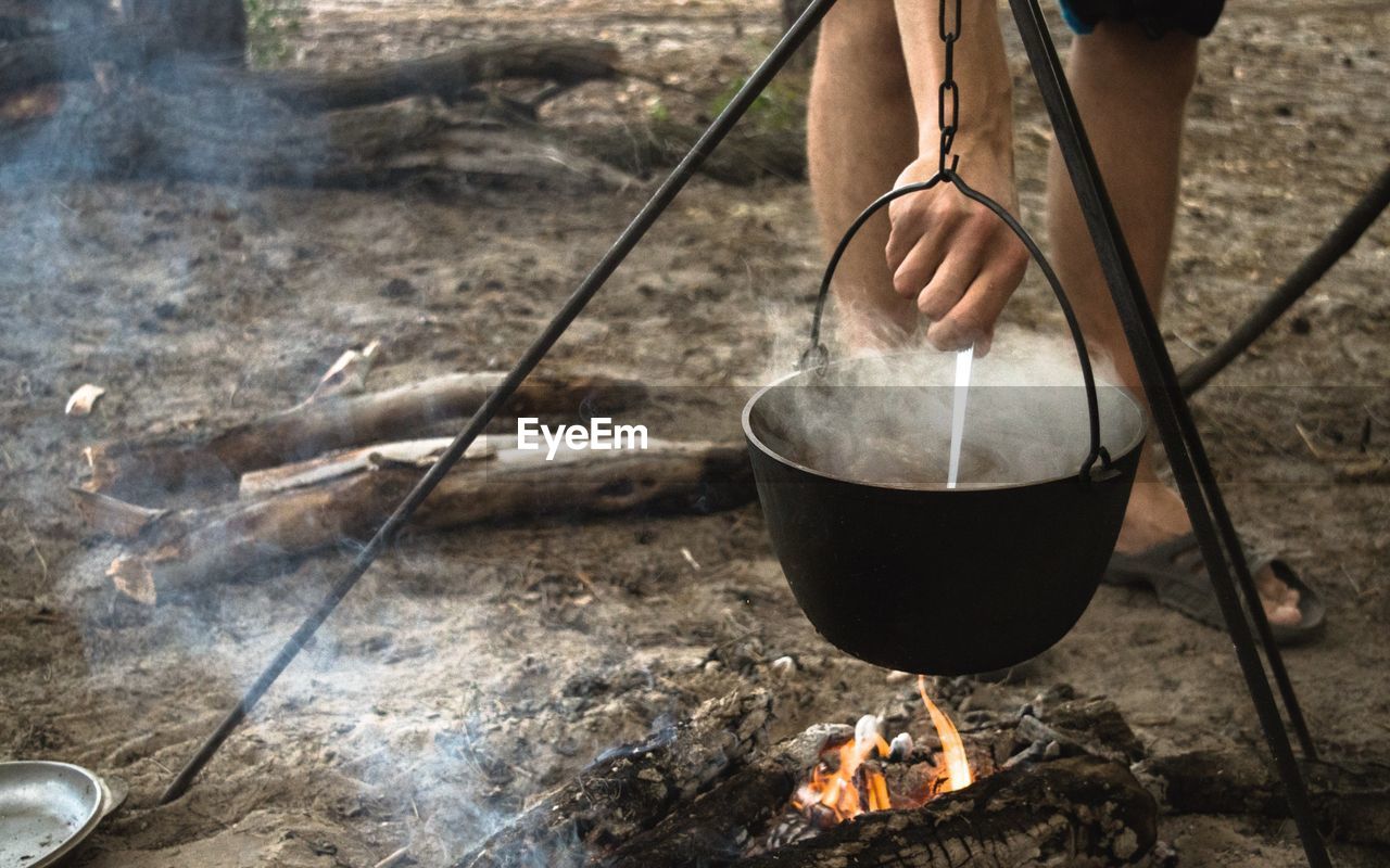 Low section of person preparing food at campfire