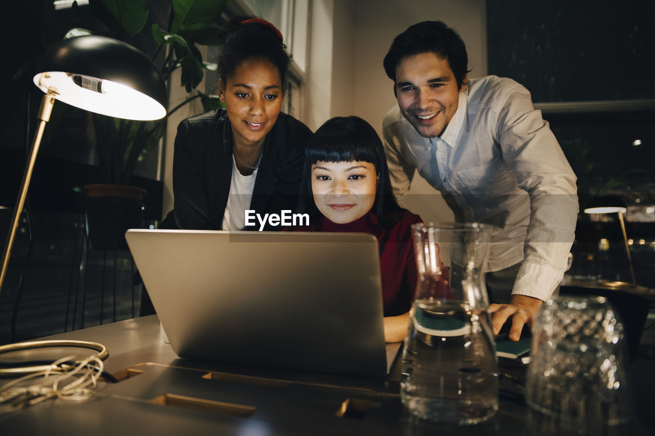 Smiling business colleagues planning strategy over laptop while working late at creative office