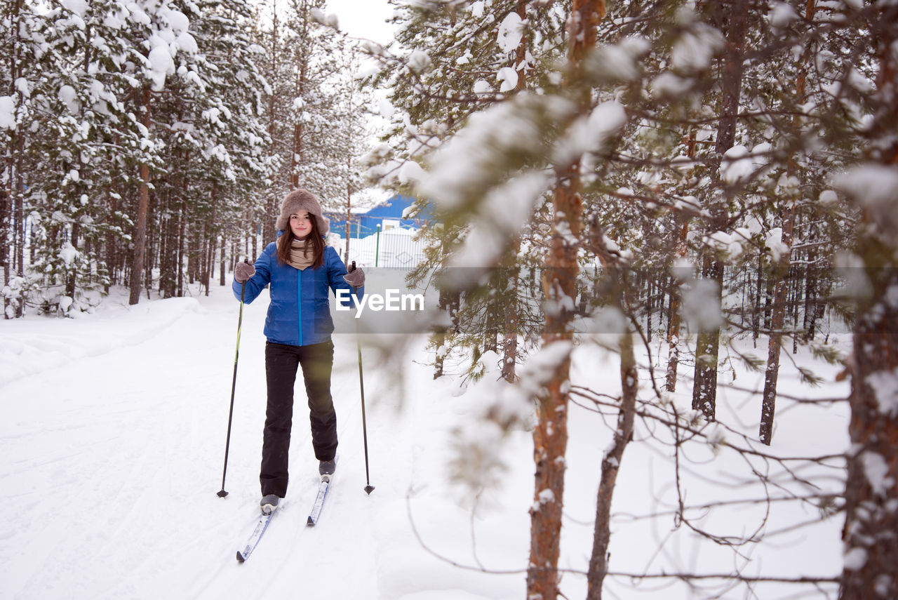Woman skiing on snow against trees