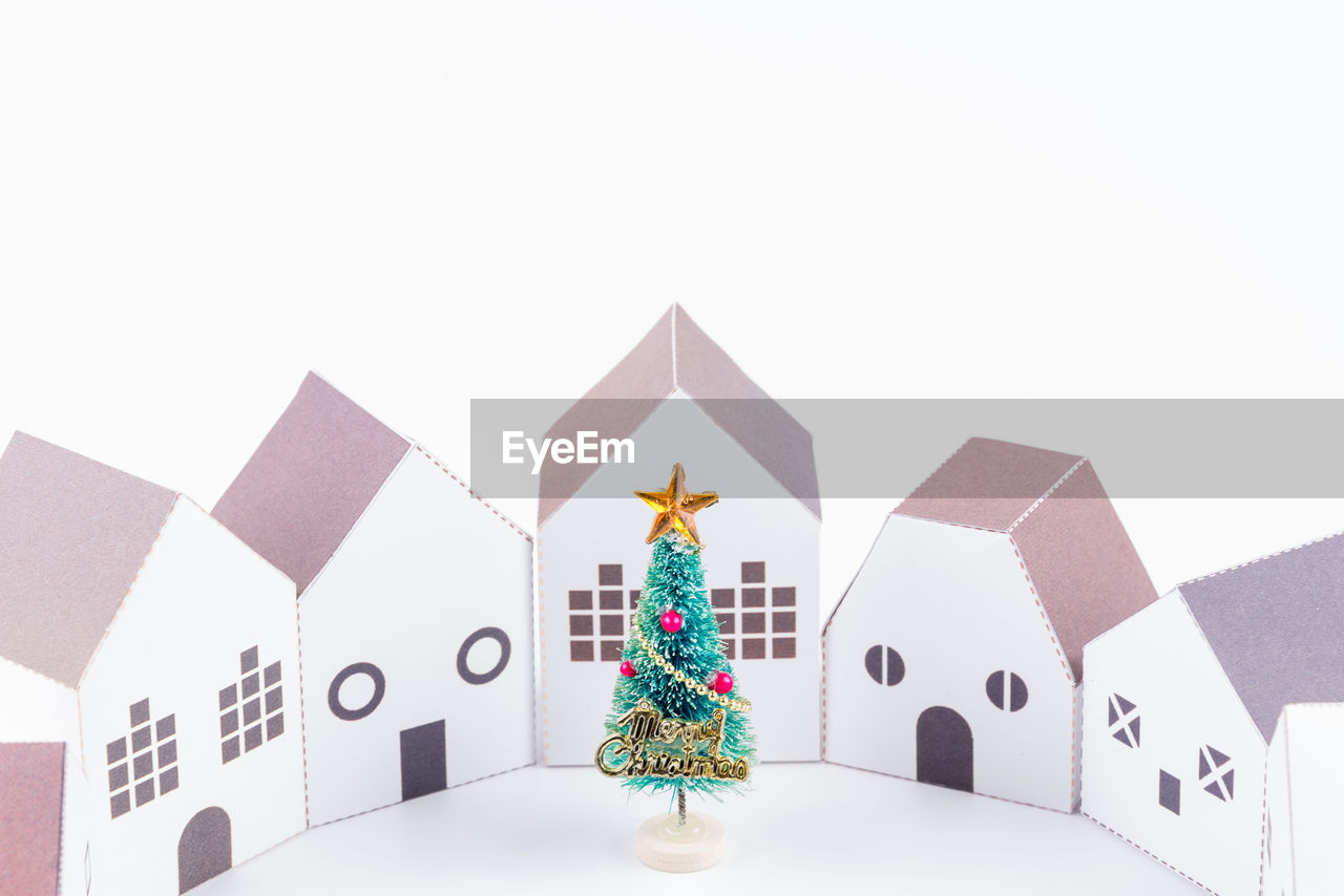 Close-up of christmas tree with model houses against white background