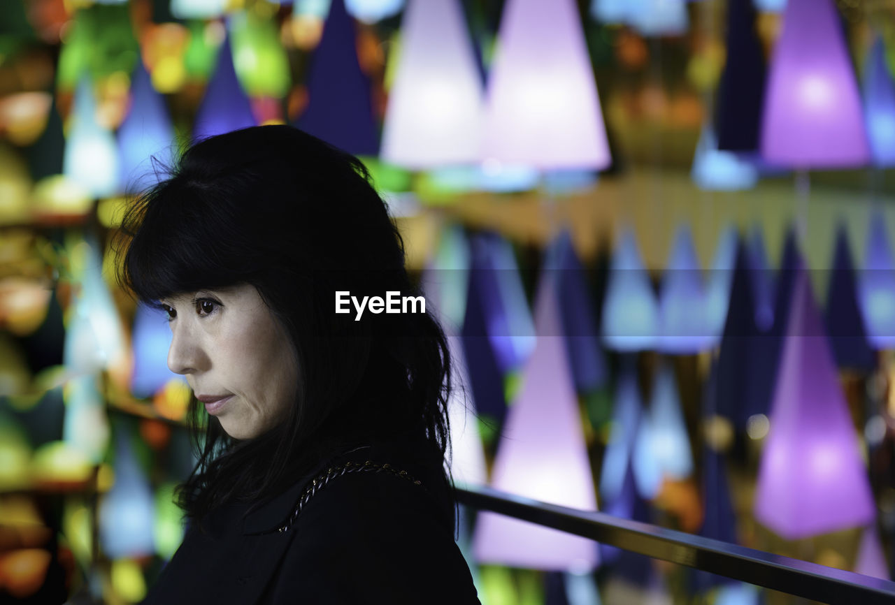 Close-up of woman looking away against illuminated multi colored lights