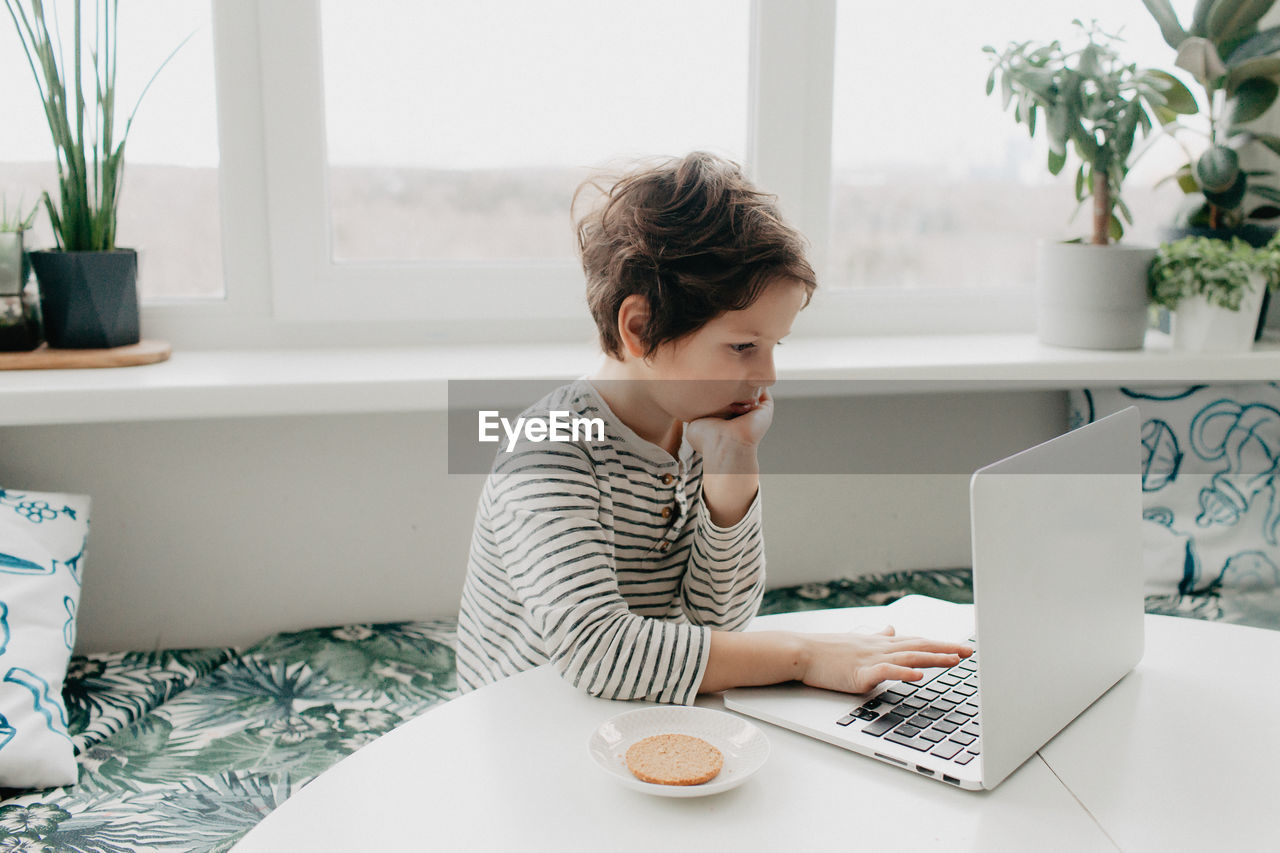 Little boy siting at the kitchen and look at the laptop. high quality photo