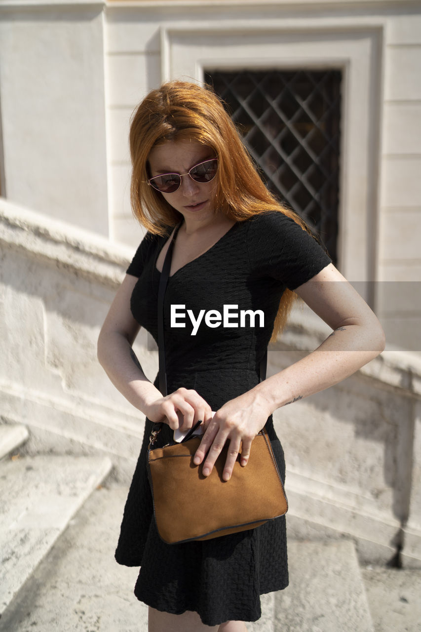 Red hair woman in black dress putting the phone back in her brown bag