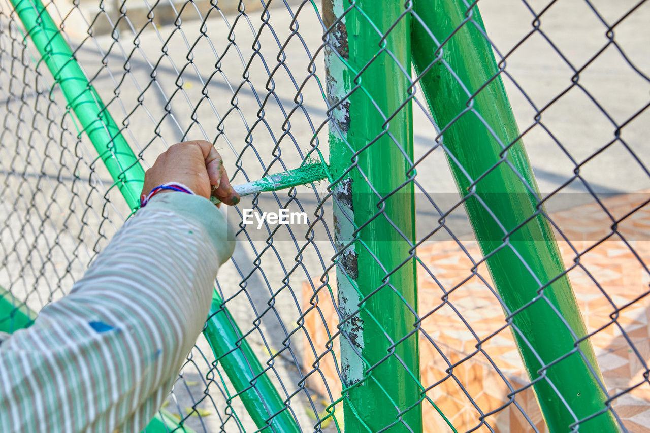 green, one person, chain-link fencing, fence, net, day, chainlink fence, blue, lifestyles, leisure activity, low section, metal, outdoors, personal perspective, nature, men, human leg, mesh, adult, close-up, security, standing, protection, sports