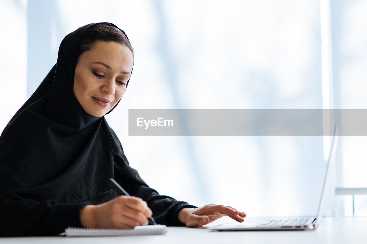 portrait of young woman using laptop while standing against sky