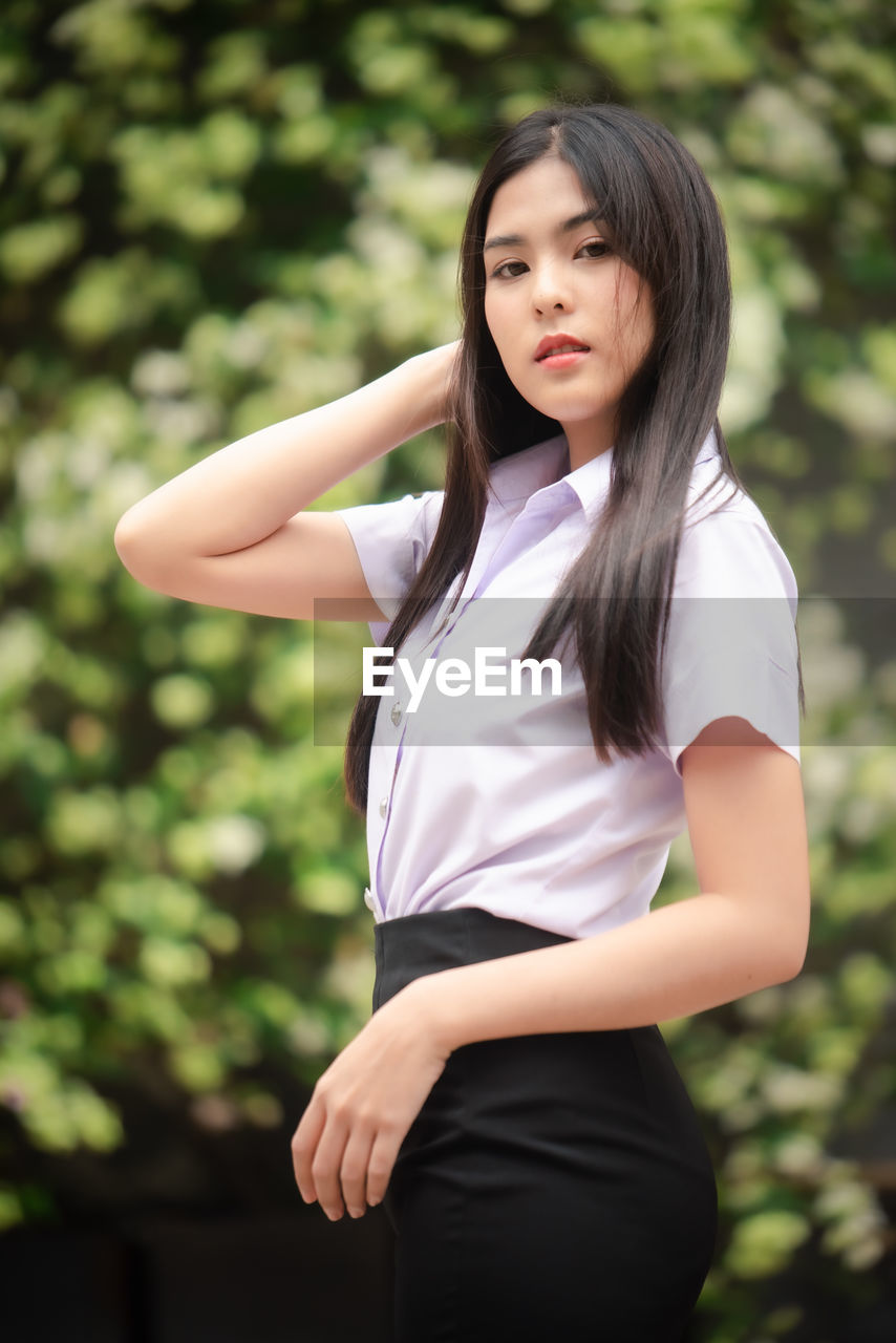 BEAUTIFUL YOUNG WOMAN STANDING AGAINST TREES