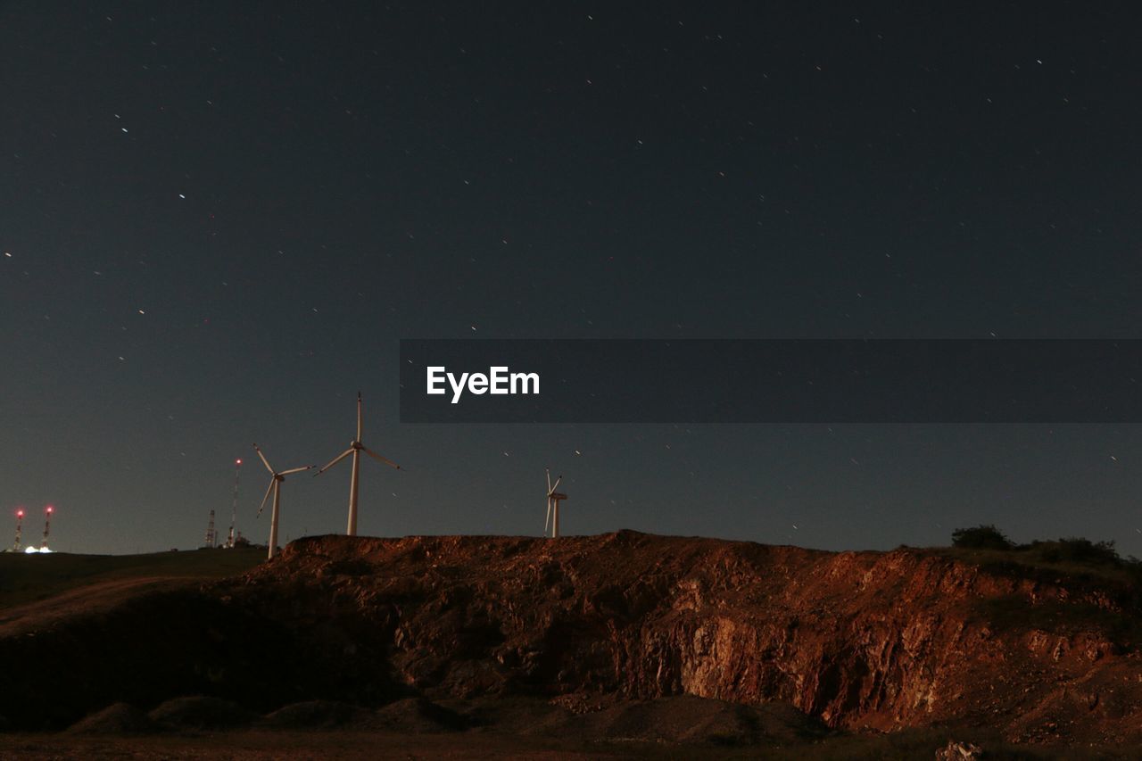 Windmills on landscape against star field at night
