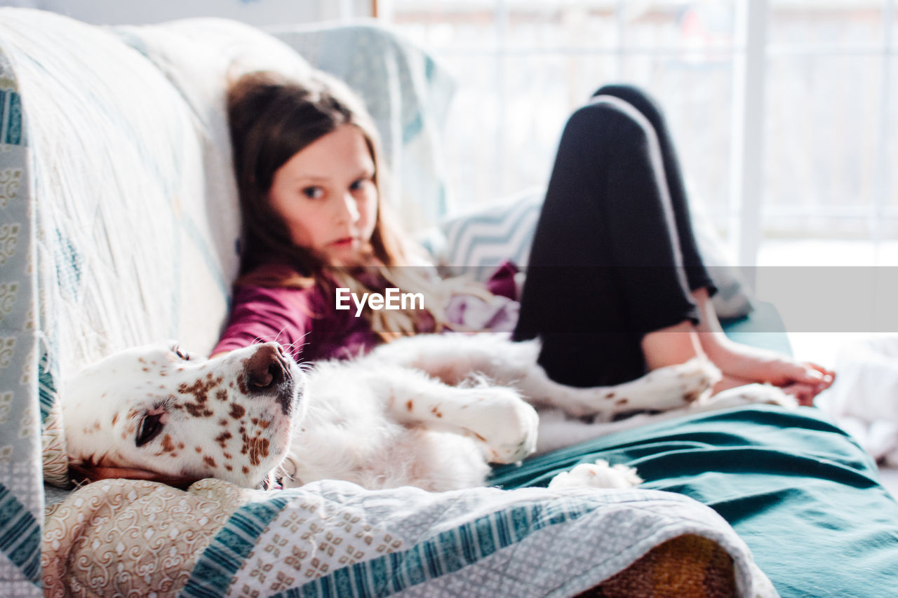 Cute girl with dog leaning on sofa at home