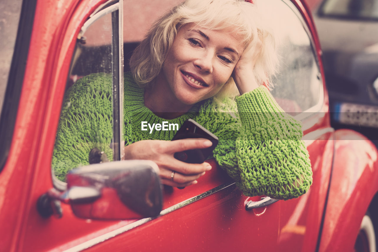 Smiling woman using mobile phone while sitting in car