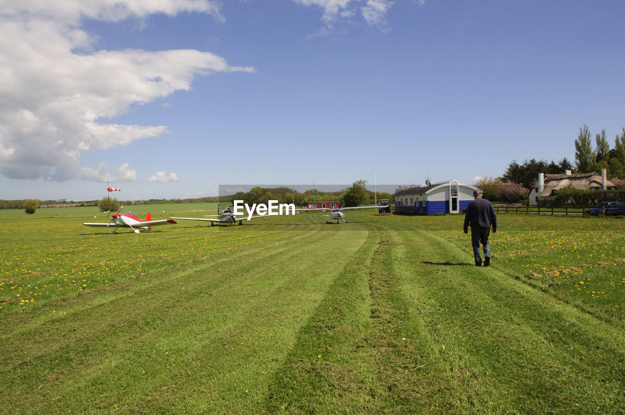 Rear view of man walking on grassy airfield
