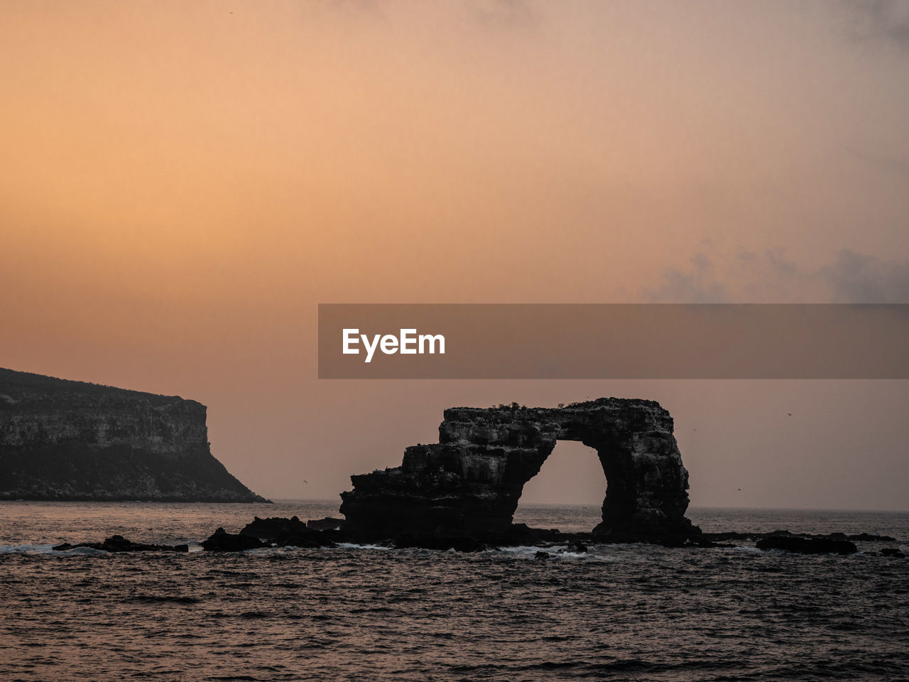 Rock formation in sea against sky during sunset