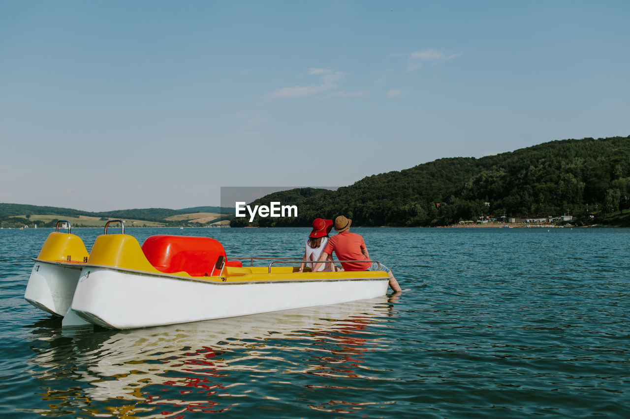 Rear view of man and woman in paddleboat on lake against sky