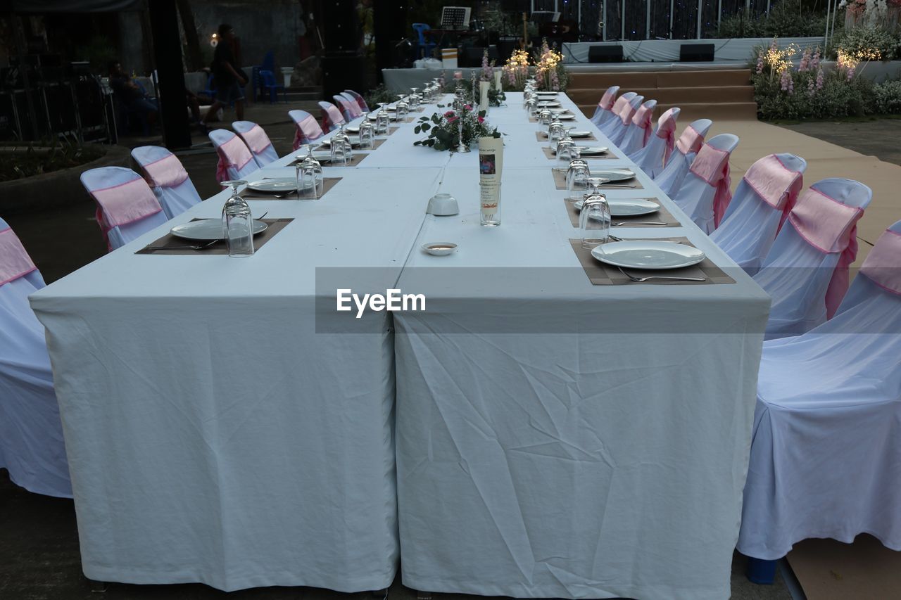 banquet, tablecloth, table, function hall, seat, meal, chair, ceremony, setting, linens, event, wedding, arrangement, celebration, furniture, place setting, food and drink, party, business, wedding reception, in a row, restaurant, dining table, no people, napkin, household equipment, white