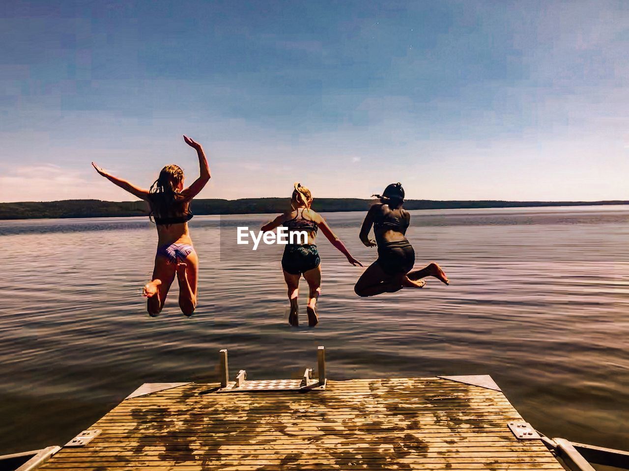 Rear view of female friends jumping in lake against sky