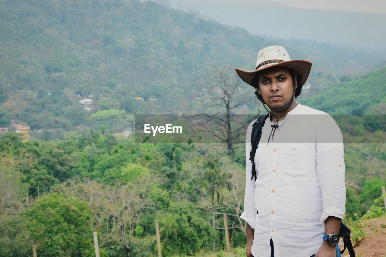 Portrait of man in hat standing against trees