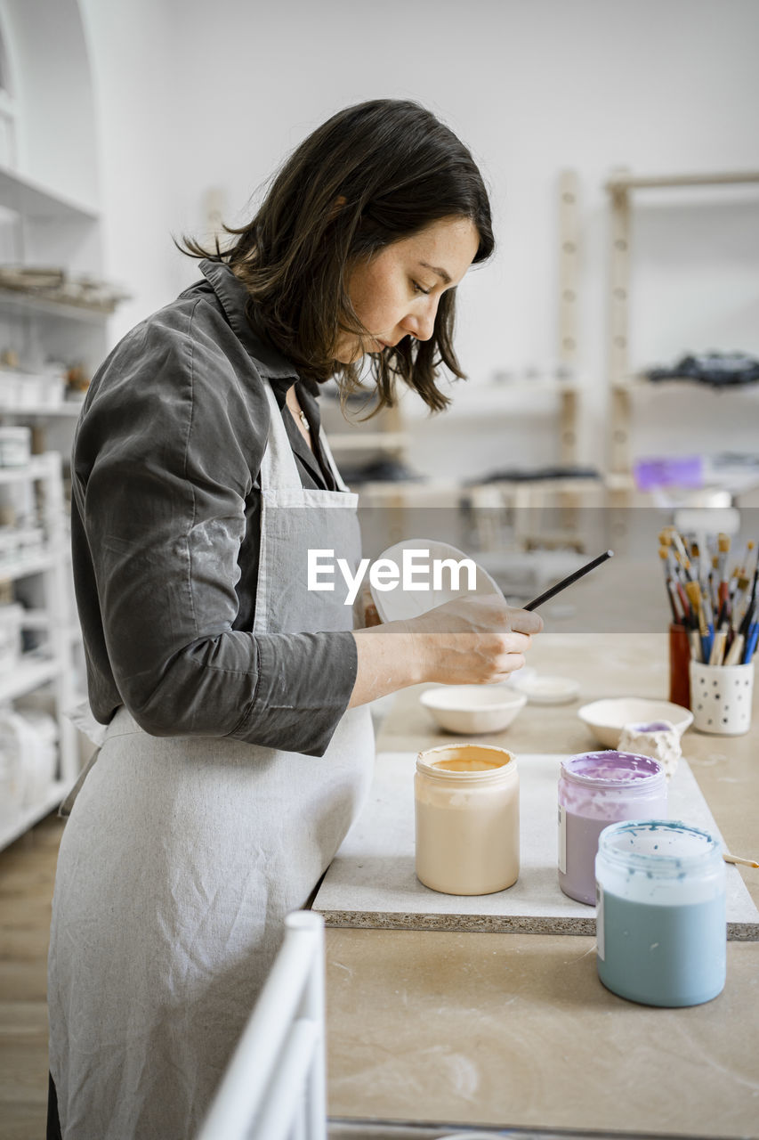 Young craftswoman painting on bowl in workshop