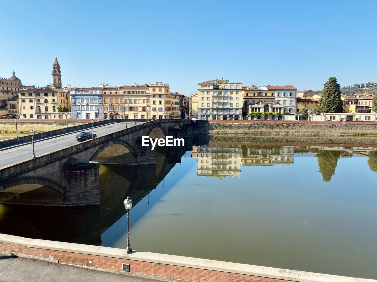 Arch bridge over river by buildings against sky in city