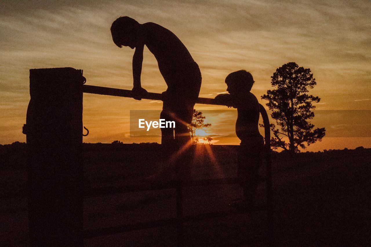 Silhouette friends playing at railing against sky during sunset