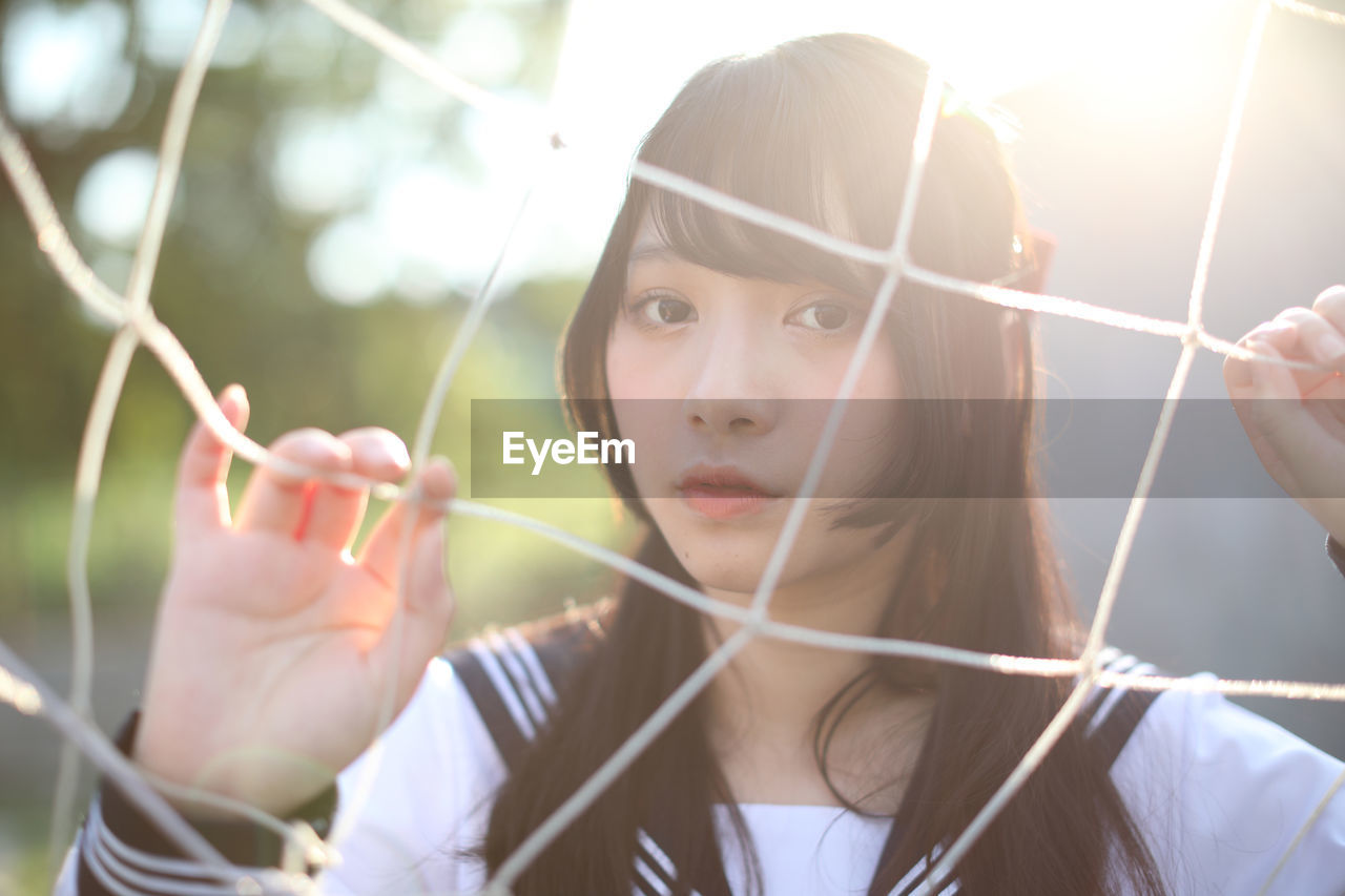 Portrait of young woman standing by sports net