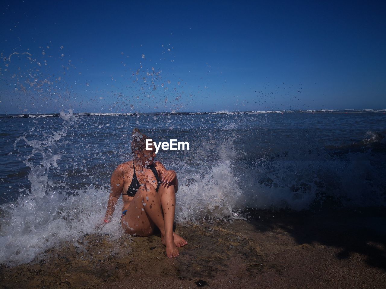 Young woman splashing water in sea against clear sky